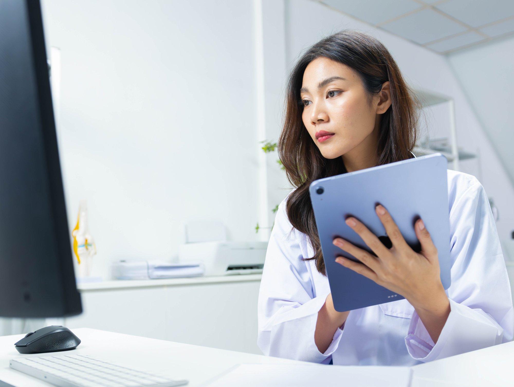 Doctor looking at computer screen while holding a tablet device